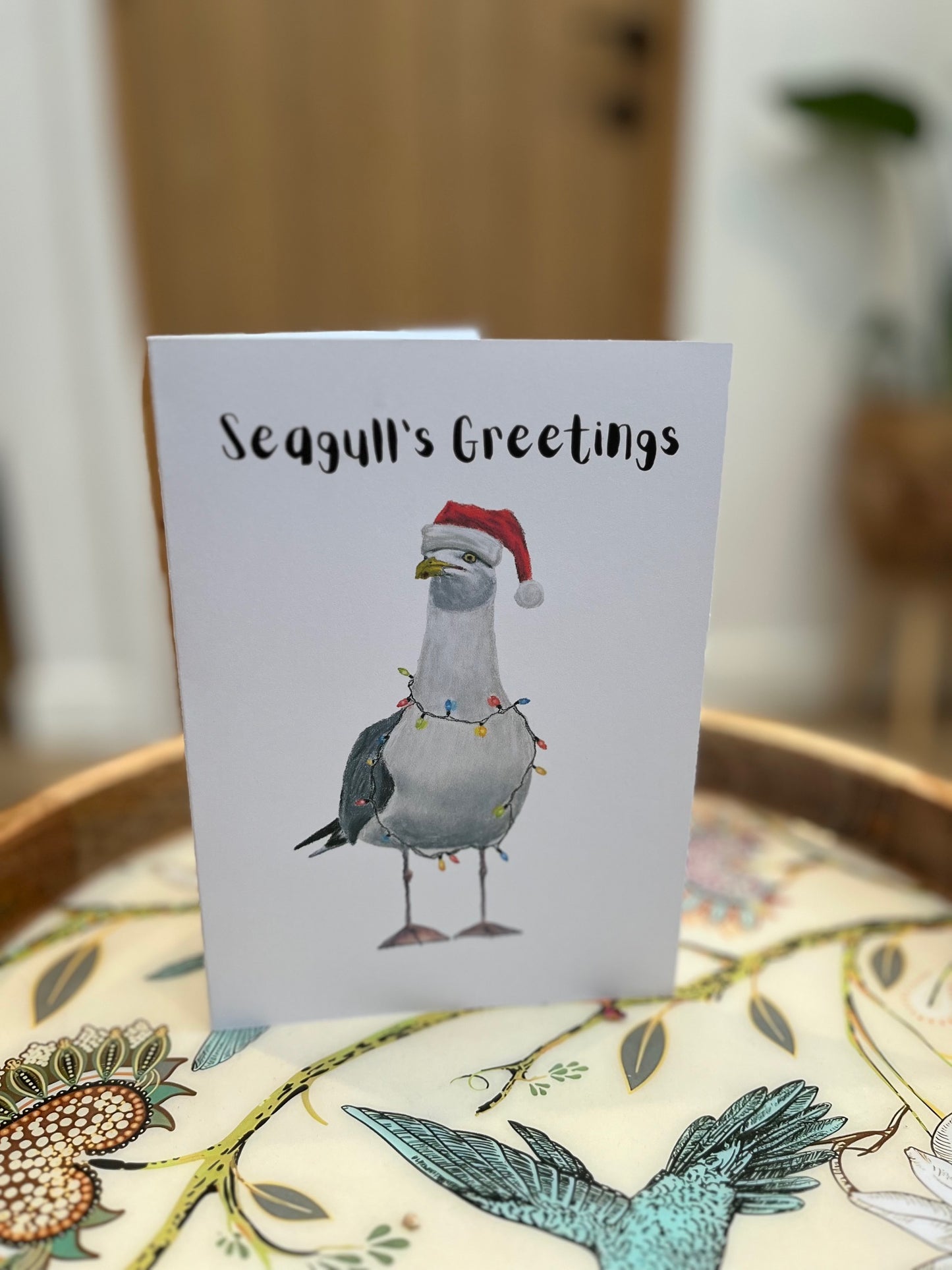 Greeting card with a seagull wearing a Santa hat and Christmas lights, on a decorative surface.