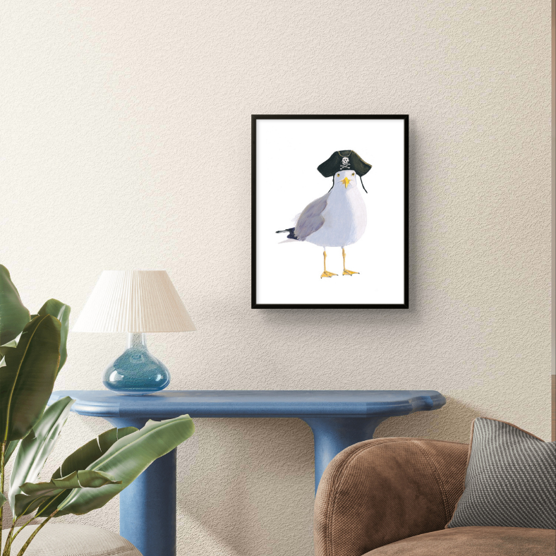 Framed artwork of a seagull wearing a pirate hat on a wall above a blue table.